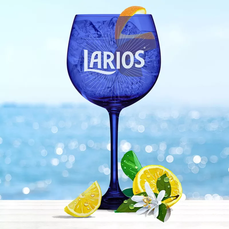 Blue Larios glass cup filled with gin tonic mediterranean and garnished with orange peels standing in front of the ocean