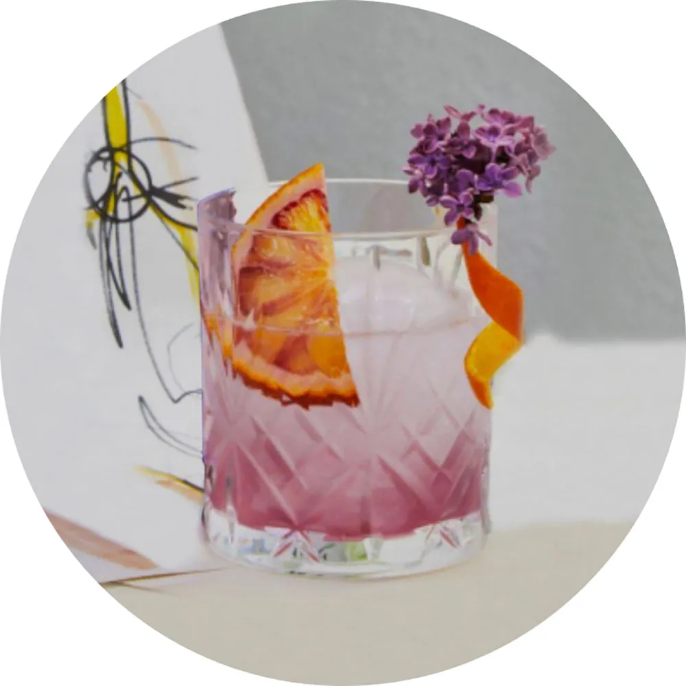 A cocktail glass filled with Larios Gin Tonic Mediterranean and garnished with a olive and a sprig of rosemary | File name: larios-gin-tonic-mediterranean-glass-garnished-2