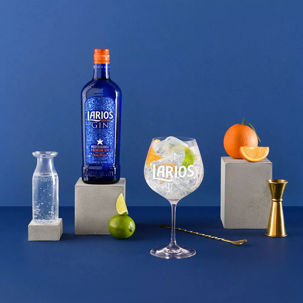A water jug, a bottle of Larios Gin and an orange standing on a concrete blocks. A measuring cup, lime and Larios glas standing infront of the concrete blocks