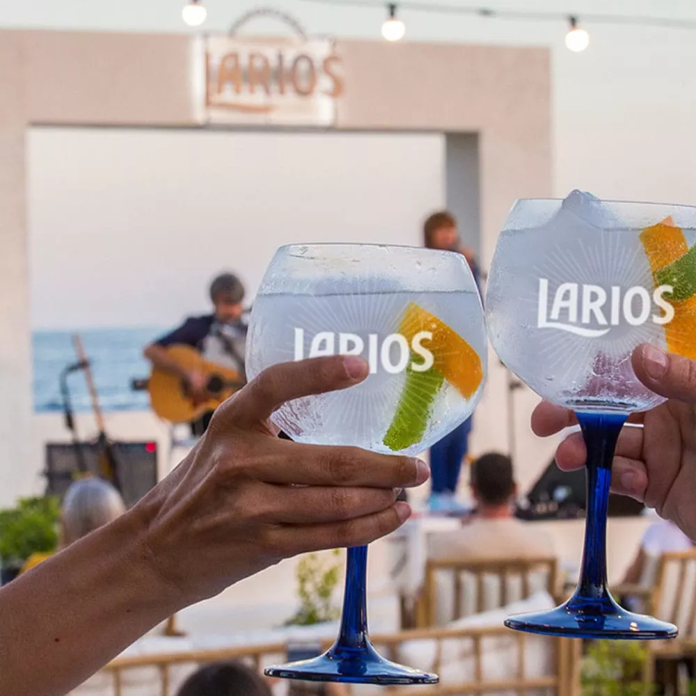 Friends toasting with two glasses of Larios Gin Tonic Rose infront of a concert at the ocean
