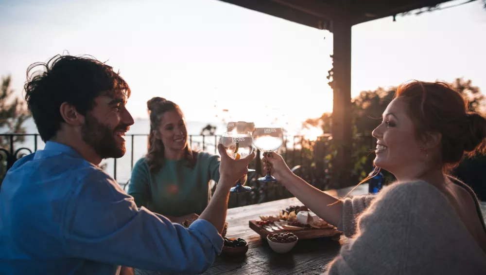 Three friends cheering their Larios drink glasses in sunset.